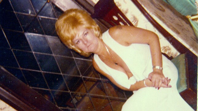 A vintage photo of a woman sitting on a chair, wearing a long white dress