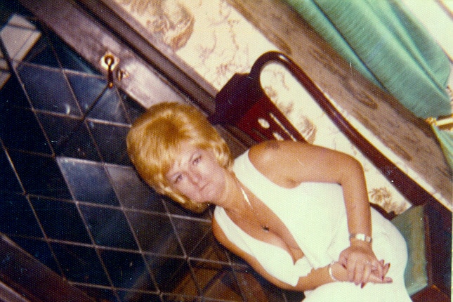 A vintage photo of a woman sitting on a chair, wearing a long white dress