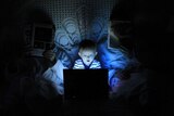 A young boy is illuminated by a computer screen in bed