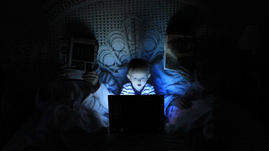 A young boy is illuminated by a computer screen in bed