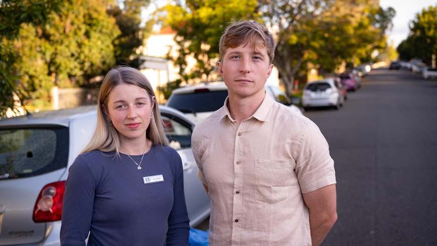 A young woman and man stand next to a vandalised car