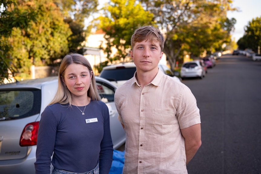 A young woman and man stand next to a vandalised car