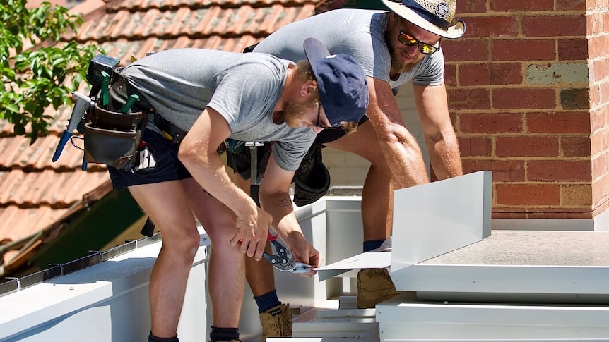 A picture of two men holding tools and working on a roof.