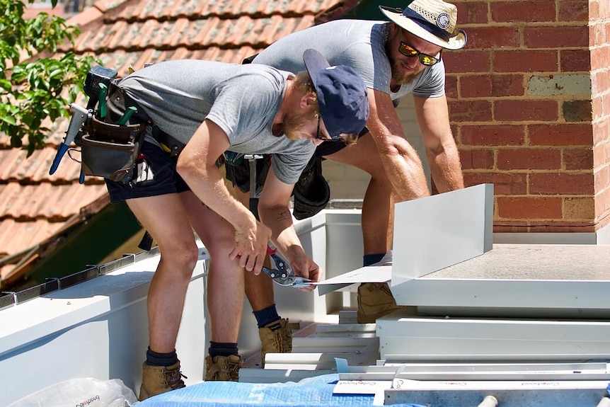 A picture of two men holding tools and working on a roof.