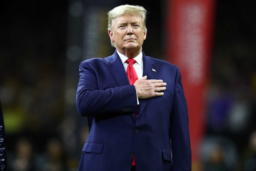 Donald Trump in a suit with his hand over his heart