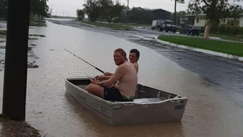 An image showing two men in a boat in water on a road, funnily holding a fishing rod.