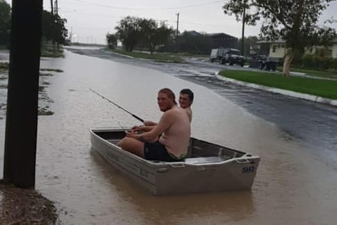 An image showing two men in a boat in water on a road, funnily holding a fishing rod.