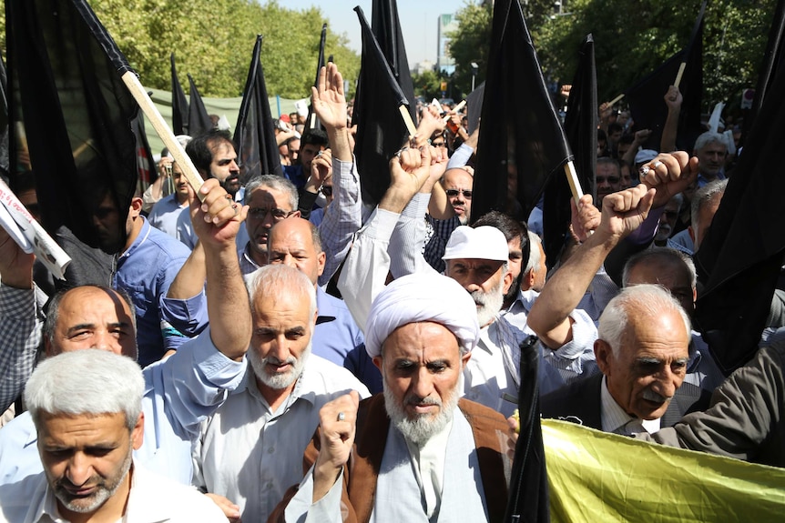 Iranian protestors shout slogans while holding black flags