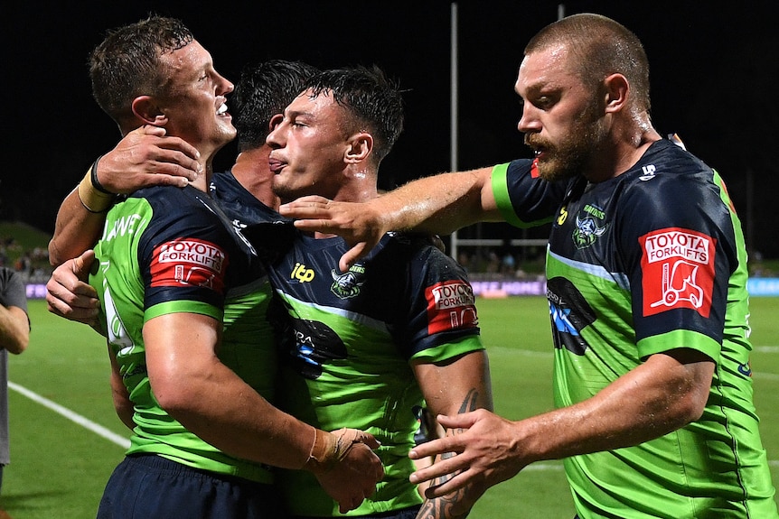 An NRL player is hugged by his teammates after recording a try.