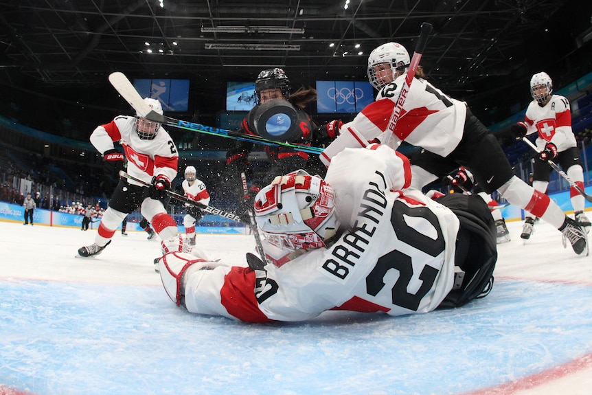 A goalie lays on the ice as attackers and defenders converge on her