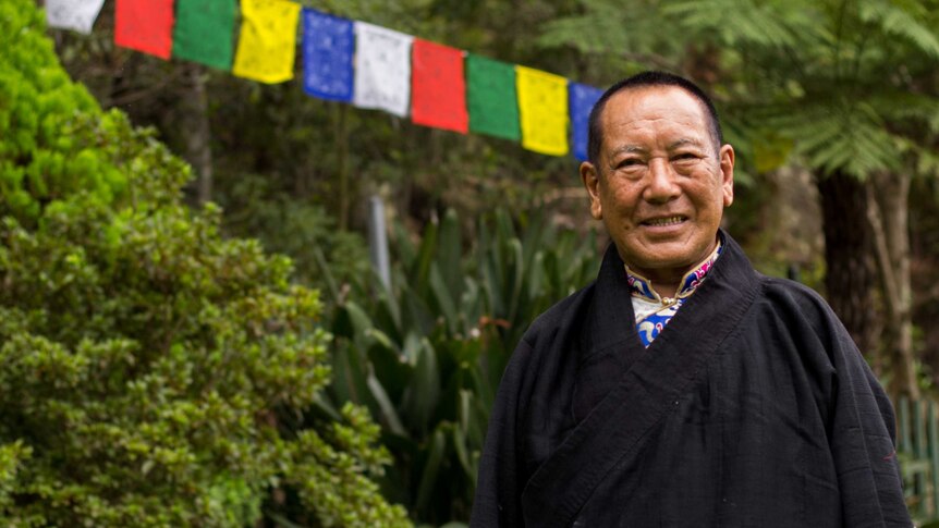 A portrait of Tenzin Paljor with a Tibetan prayer flag in the background.