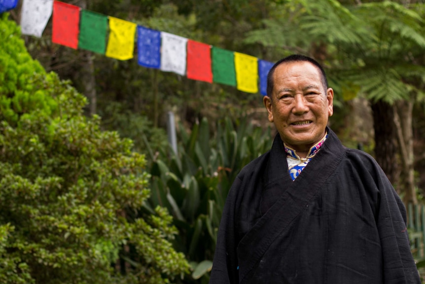 A portrait of Tenzin Paljor with a Tibetan prayer flag in the background.