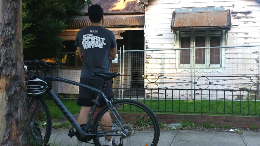 A man stands in front of a dilapidated house in Sydney.