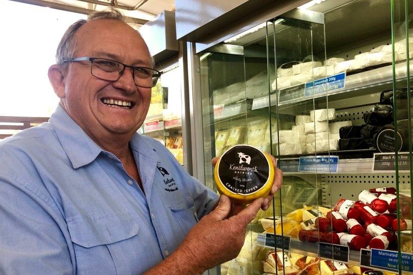 John Cochrane holding a waxed cheese in front of the cabinets of cheese.