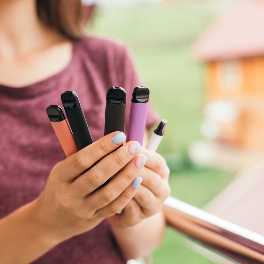 A woman holding several coloured disposable vapes.