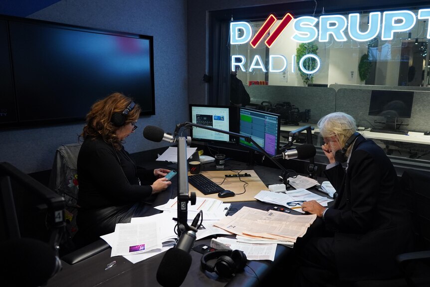 Libbi and Bob sitting in a radio studio in front of microphones, D//srupt Radio sign in window.