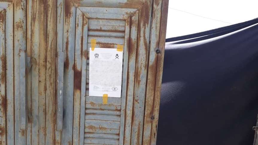A sheet of paper with writing and a letterhead, which has been taped to a metal, rusted door.