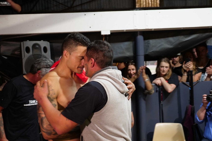 Lou Brown hugs a large Maori man with facial tattoos.