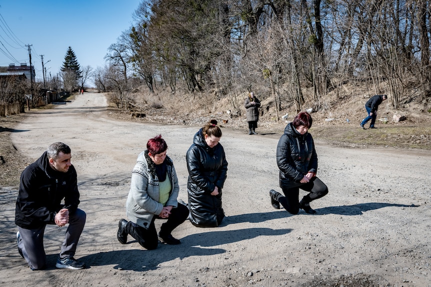 Four people on their knees on a dirt road 