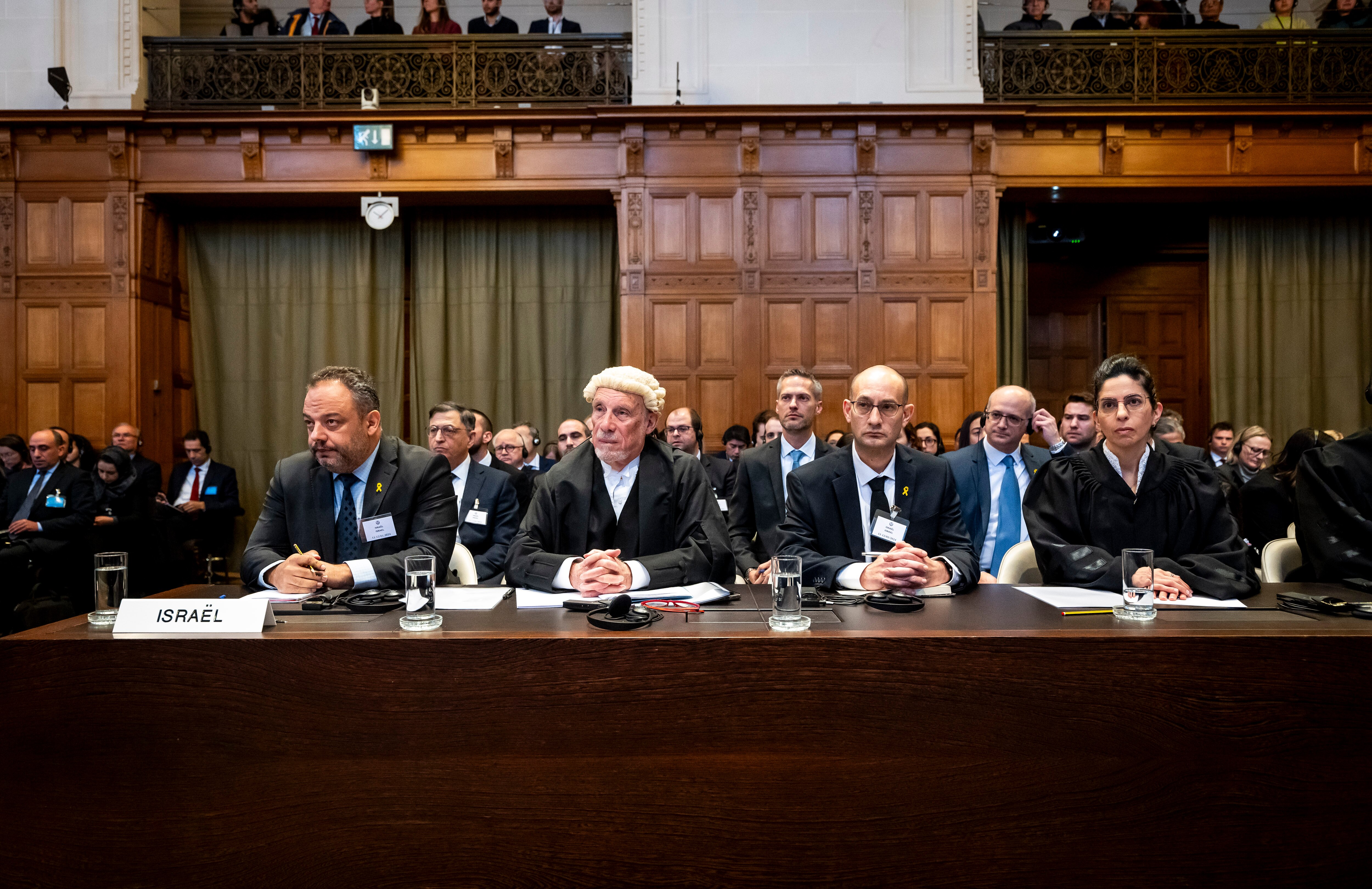 Israeli advocate Galit Rajuan, with brown hair, black cloak and white neck tie, sits at wooden desk in large room looking ahead.