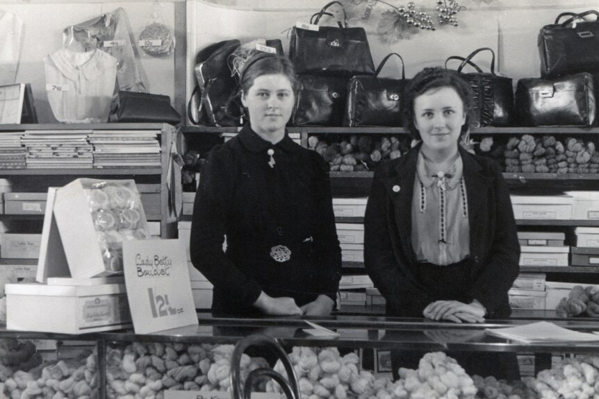 two women gently smile with their hands crossed on a counter in a shop selling handbags and other goods