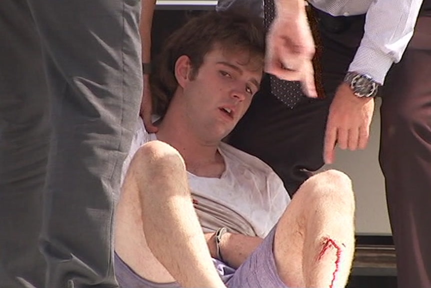 Ryan John Howes arrested sits on the ground, surrounded by police