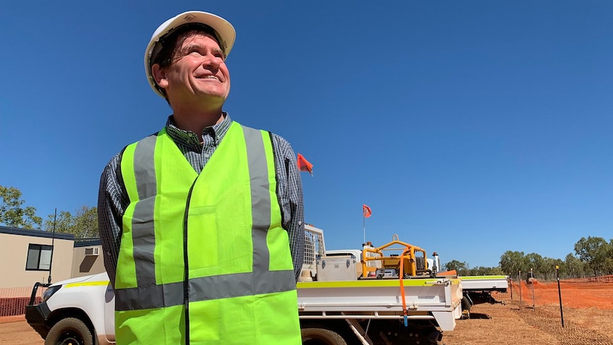 A man, wearing a hard hat and a high viz vest, stands at a solar project in the NT