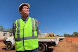 A man, wearing a hard hat and a high viz vest, stands at a solar project in the NT