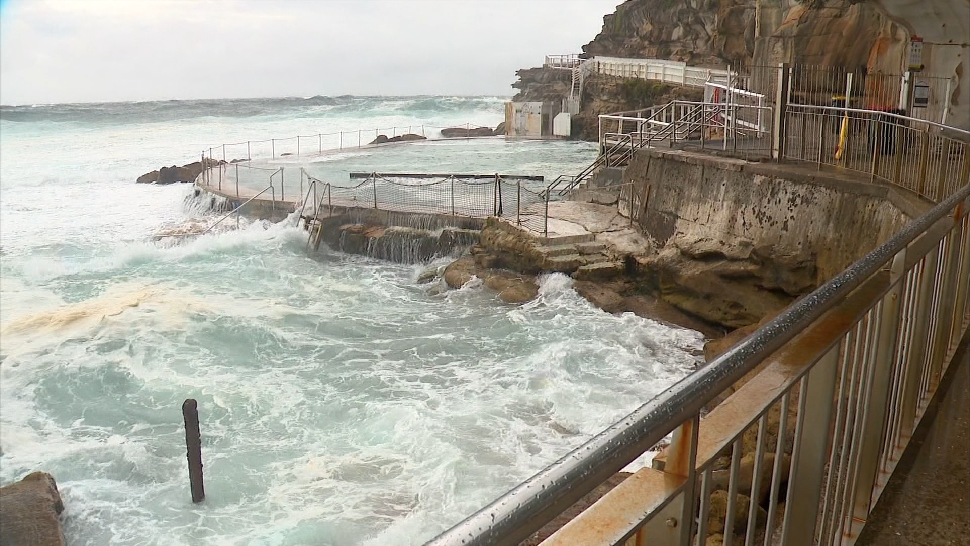 Inquietas olas oscuras chocan contra un estanque de rocas en una playa de Sydney.