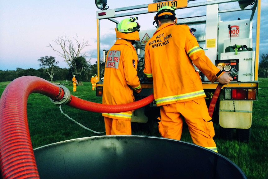 Volunteer firefighters practice using a hose and fire engine.