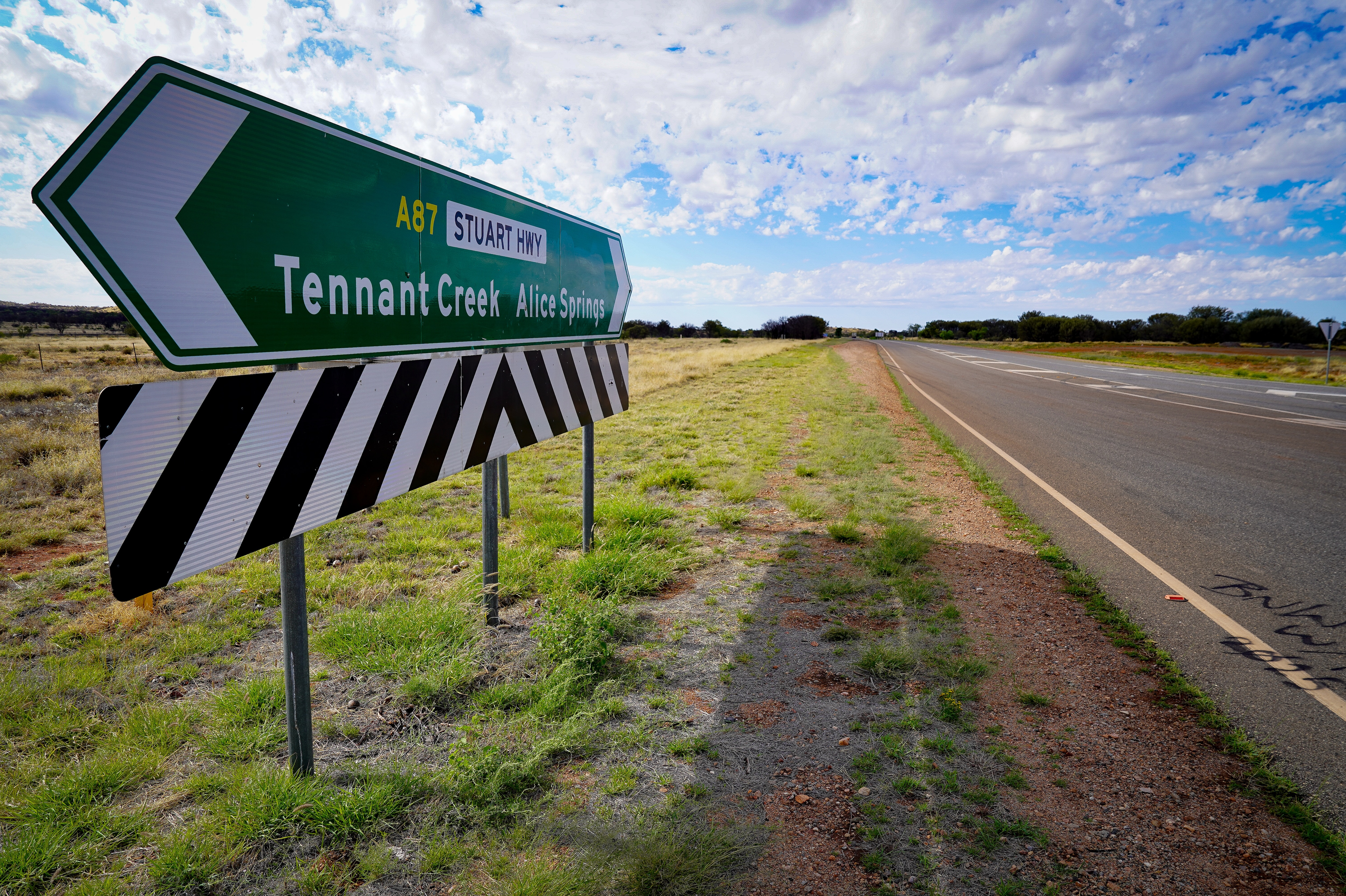 Una señal de tráfico en una carretera que apunta a Tennant Creek en una dirección y Alice Springs en la otra dirección.