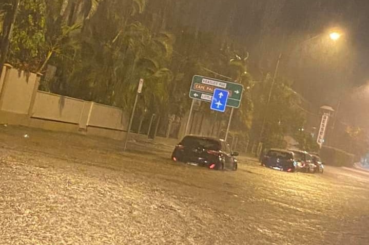 Rain pours on a flooded night time street in Townsville. A number of cars sit in the water. It is up to their wheels.