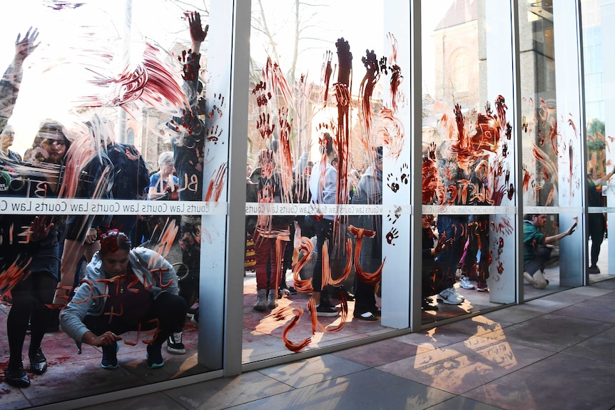 People spread red ochre over windows at the NSW Supreme Court during a protest over the death of 14-year-old Elijah Doughty.