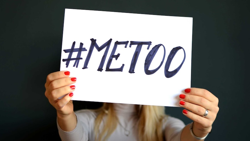 A woman holding a sign in front of her face that says #METOO.