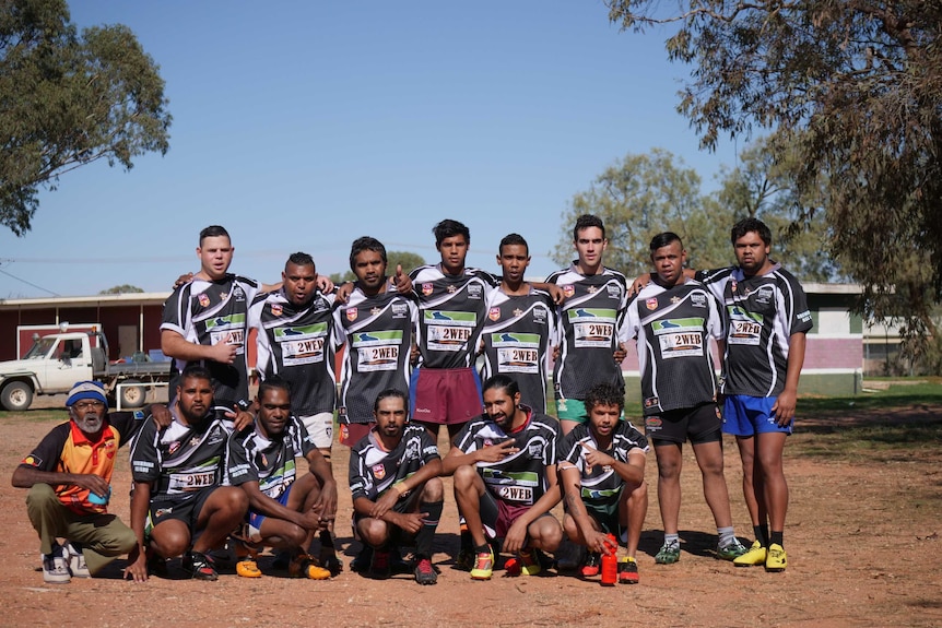 A group of football players wearing jerseys and shorts stand for a group photo next to an oval.