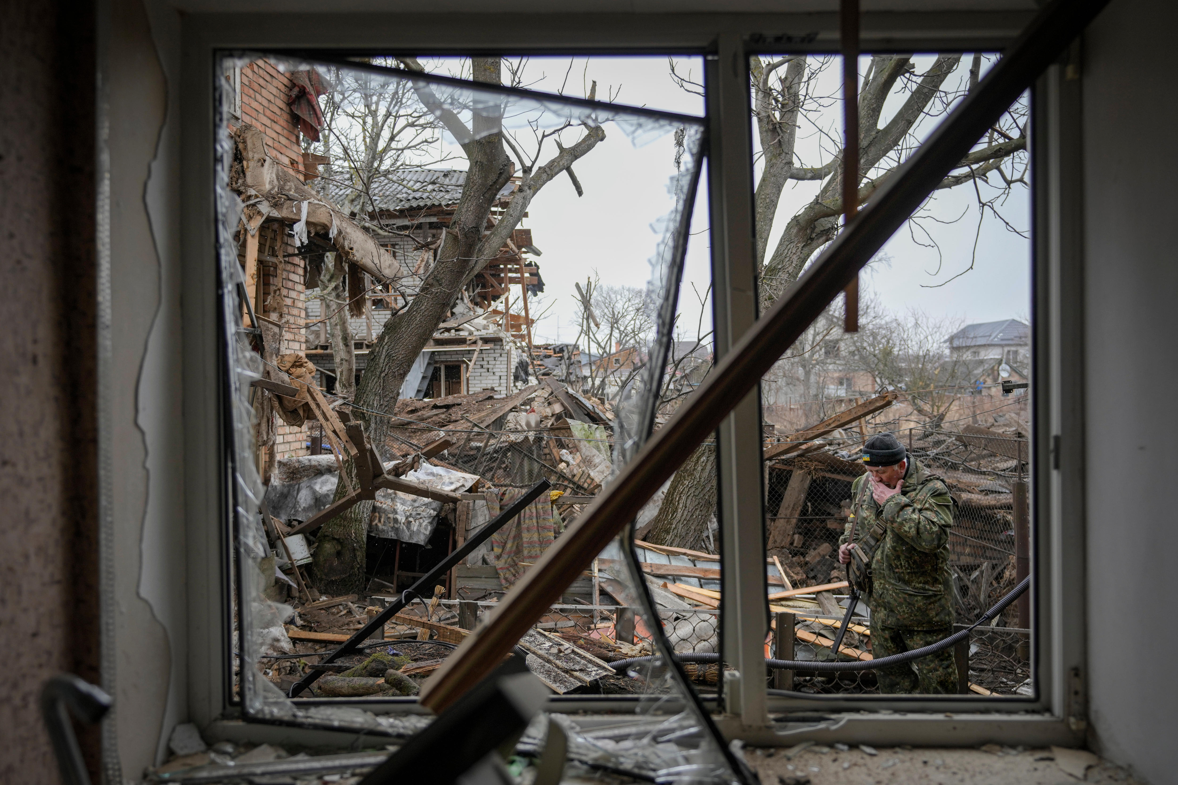 A member of territorial defense wipes his face in the backyard of a house that was damaged by a Russian airstrike.