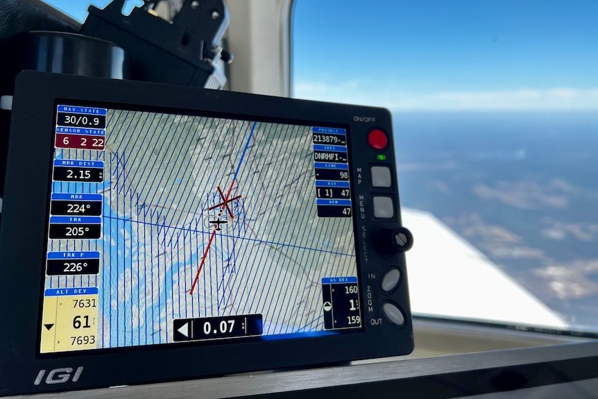 Focus on computer screen inside plane showing elevation data, with blurred view of Tweed landscape in background.