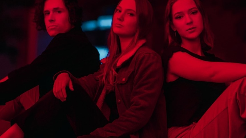 a man and two women sit next to each other with serious expressions, a red glow over them