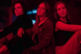 a man and two women sit next to each other with serious expressions, a red glow over them