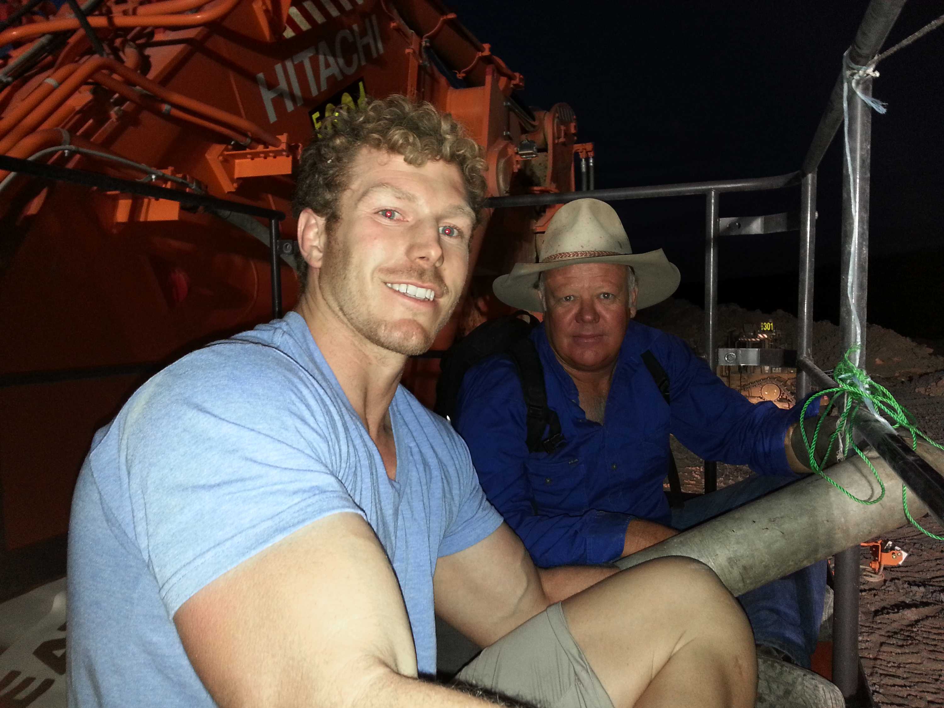 Two men sit on a large piece of plant equipment at night.