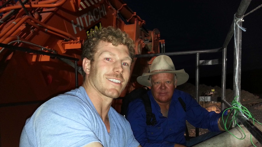 Two men sit on a large piece of plant equipment at night.