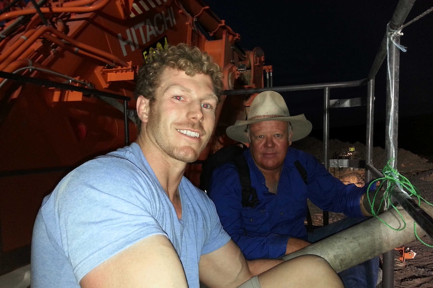 Two men sit on a large piece of plant equipment at night.