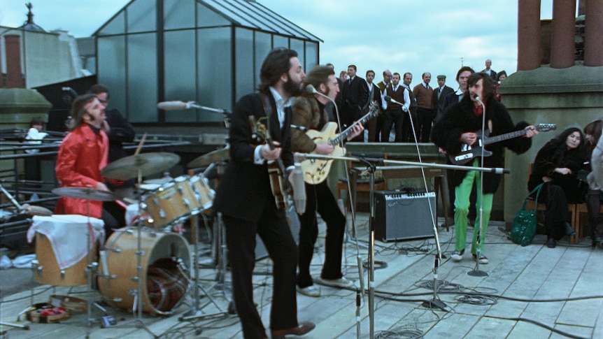 A photo of the Beatles band playing on a rooftop beneath grey skies