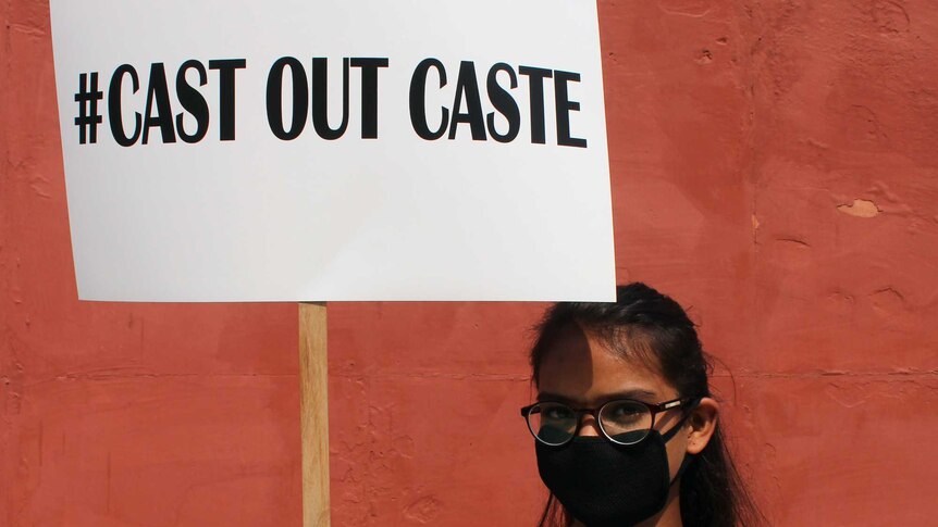 A demonstrator holds placard stating 'CAST OUT CASTE' protesting against increasing atrocities on Dalit community