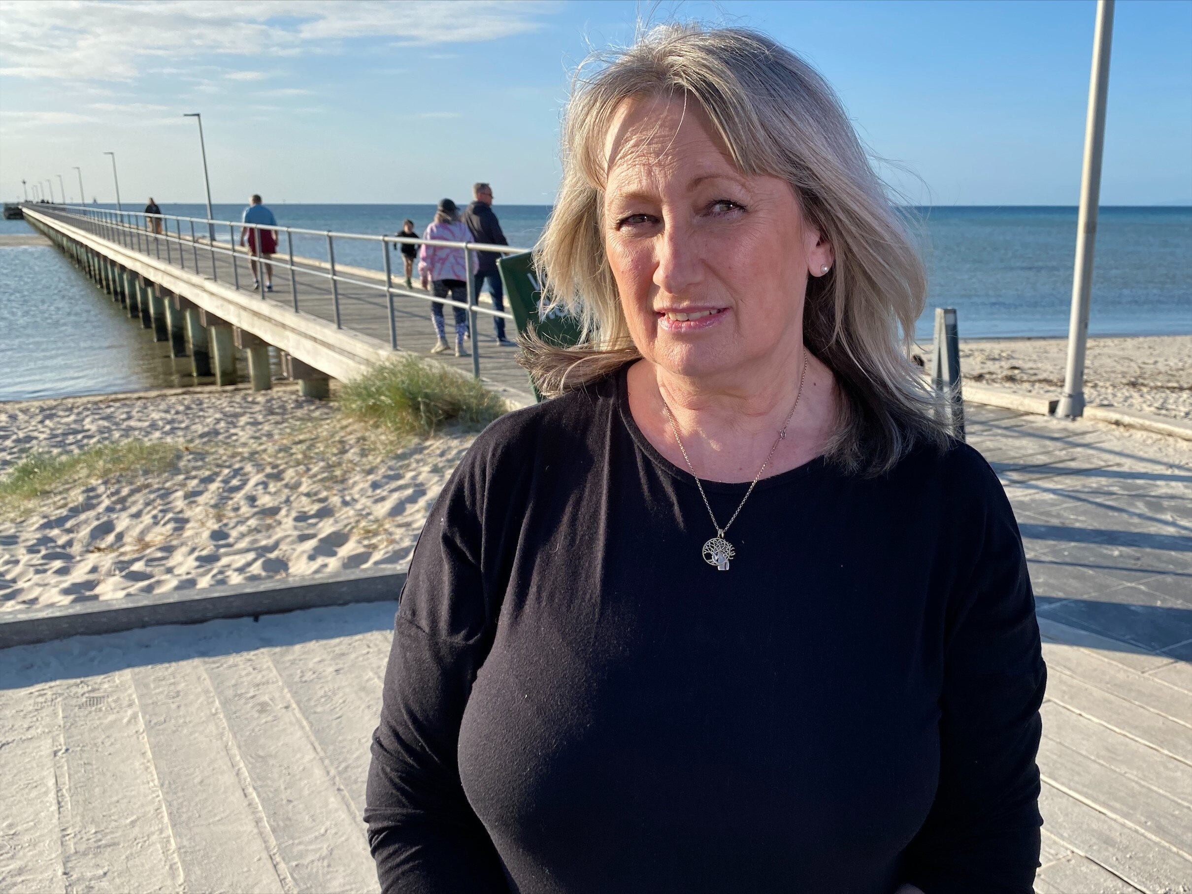 A blonde-haired woman wearing a black shirt looks into the camera while at the beach.