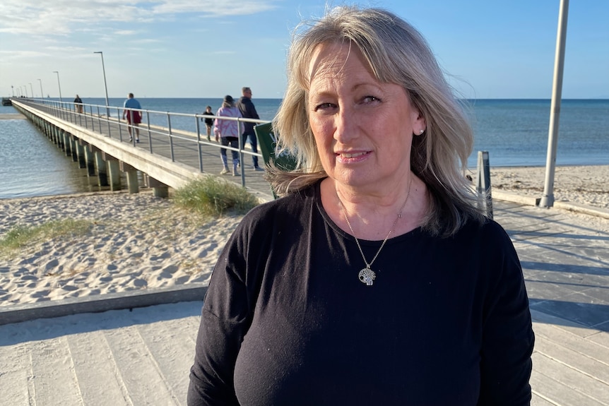 A blonde-haired woman wearing a black shirt looks into the camera while at the beach.