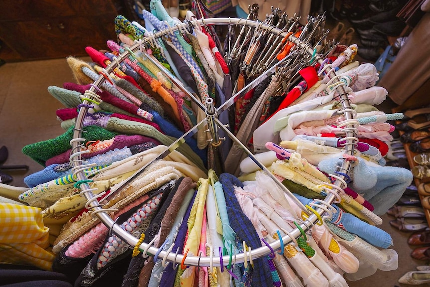 Knitted shirts and jumpers of all colours hang off a circular metal rack in the middle of a shop floor.