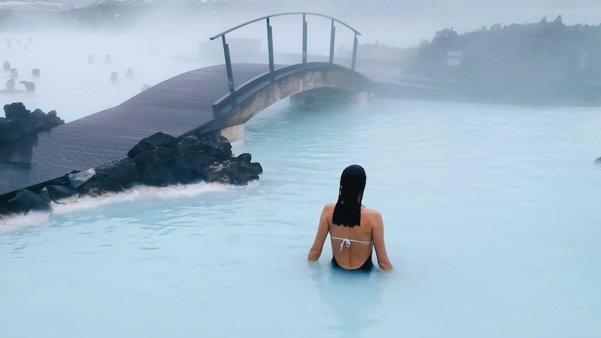 Woman in bathing suit standing in Iceland's blue lagoon for a story about travel destinations to visit if you love winter.