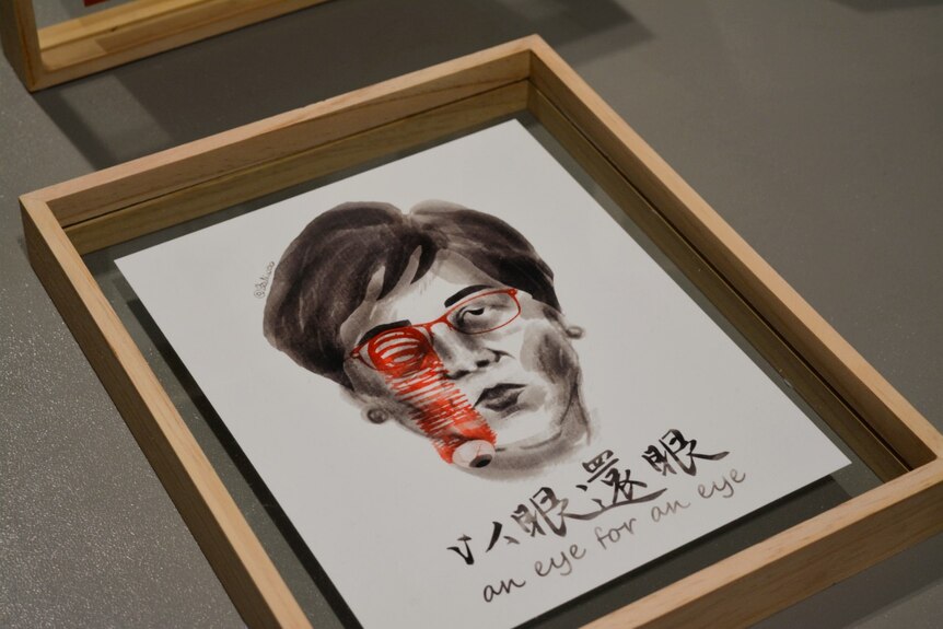 A watercolour illustration of Carrie Lam with glasses and a popped eyeball sits in a transparent wooden frame.