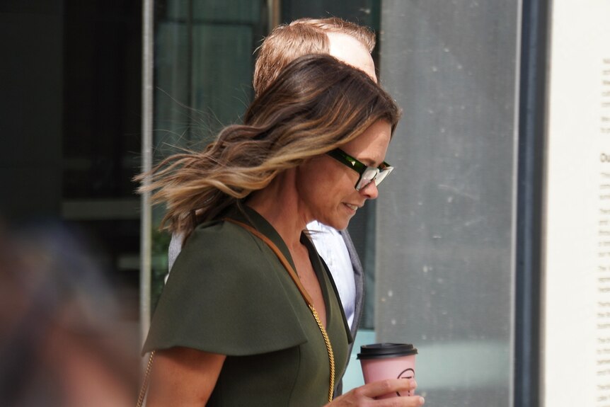 A woman in a green shirt walks along a path holding a coffee